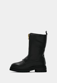 Bota de cuero negra a media pantorrilla con suela gruesa, cremallera dorada en la parte delantera y tira en la parte trasera, mostrada de perfil sobre un fondo blanco.