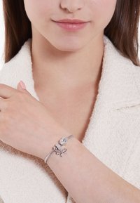 Pulsera de plata con intrincados charms: un cubo adornado con cristales y un diseño de lazo, montados en una banda flexible y texturizada.
