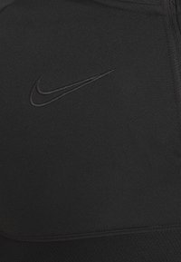 Schwarzes, zipfähiges Sportoberteil mit einem dezenten, gestickten Nike-Logo. Glattes Material mit unterschiedlichen Texturen an den Schultern und am Körper.