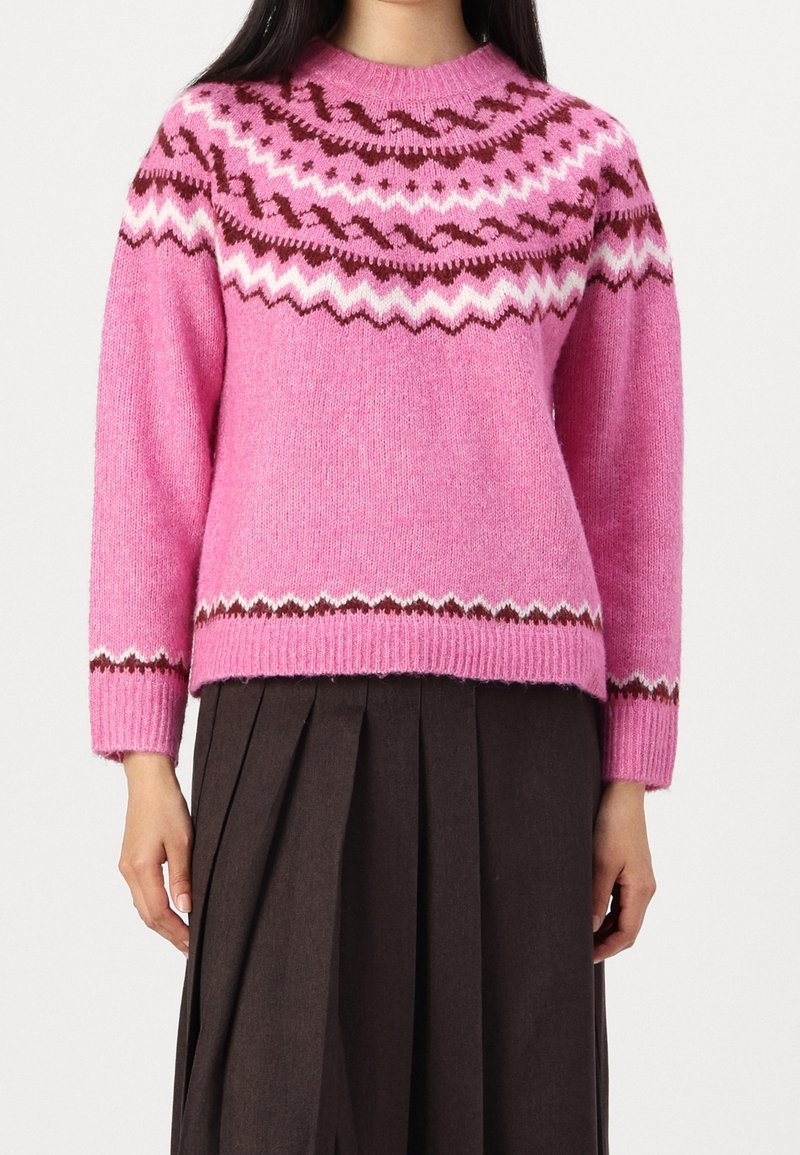 Stickad rosa tröja med rund halsringning, prydd med bruna och vita mönstrade detaljer på oket och ärmarna. Bärs över en mörk plisserad kjol.