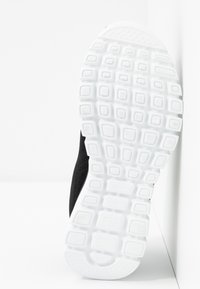 Schwarzer Sneaker im Profil mit einem strukturierten schwarzen Obermaterial und einer weißen Gummi-Außensohle mit einem gemusterten Profil für besseren Grip.