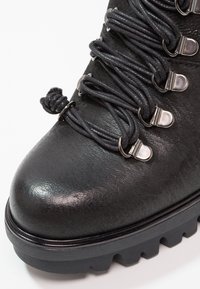 Gros plan d'une chaussure de randonnée en cuir noir avec une semelle épaisse à crampons et des lacets ronds passés dans des crochets en métal.