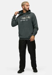 Mörkgrå huvtröja med Seattle Seahawks-logotyp, dragskohuva och framficka. Matcher med svarta cargobyxor och svarta skor.