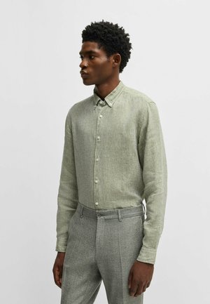 Hellgrüne Hemdjacke aus strukturiertem Stoff, langärmlig und mit Kragen, kombiniert mit grauen, strukturierten, maßgeschneiderten Hosen.
