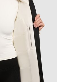 Jakna od pufera s krem unutrašnjošću i crnim vanjskim dijelom. Ima glatku teksturu, skriveni džep i elegantan dizajn.