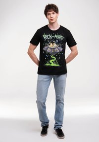 Black T-shirt with "Rick and Morty" graphic, featuring green slime and purple spaceship. Worn with light blue jeans and black sneakers.