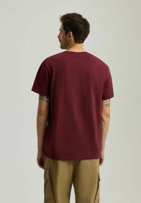 Bordowa bawełniana koszulka z luźnym krojem, krótkim rękawem i okrągłym dekoltem, noszona z beżowymi spodniami cargo. Gładka tekstura, podstawowy design.