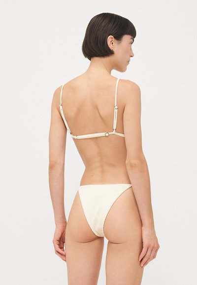 Crème-kleurige bikini met dunne bandjes en een geribbelde textuur. De achterkant heeft een decoratieve sluiting en een minimalistische snit.