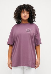 Oversized purple cotton t-shirt featuring short sleeves and a chest graphic with "Celestial Symphony Solar Eclipse" in white and black.