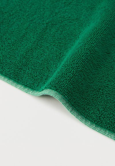 Πράσινη πετσέτα με υφή και διπλωμένη γωνία σε λευκό φόντο, που δείχνει υφαντό άκρο και βρόχους υφάσματος περκάλι.