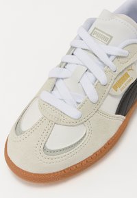 Sneakers Puma in suede grigio chiaro e pelle bianca con un accento nero. Presentano lacci bianchi e una suola in gomma rigata.