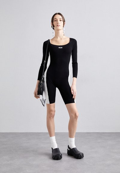 Mustaga bodysuit pikkade varrukatega, ruudukujulise kaelusega, valgete külgpaneelidega; on kombineeritud mustade puugiga jalatsite ja valgete sokkidega, hoides käes musta kotti.