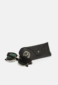 Ochelari de soare Ray-Ban cu un cadru din scoică întunecată și lentile verzi, însoțiți de o husă din piele neagră cu un logo auriu.