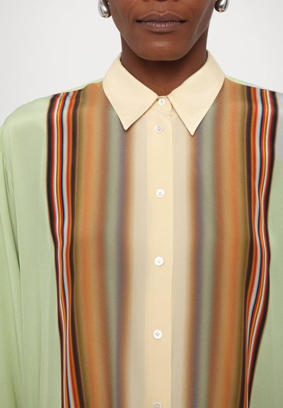 Camisa de manga larga con base verde, frente beige en contraste con rayas verticales en marrón, naranja y azul. Cierre abotonado.