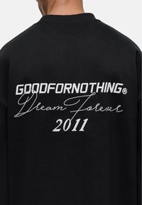 Felpa nera con testo bianco sul retro: "GOODFORNOTHING® Dream Forever 2011." Design semplice con una texture liscia.