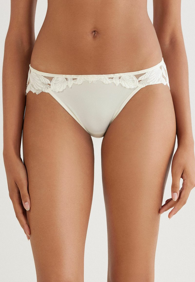 Romantische damesbikini slip in crème, met een gladde voorkant en bloemenkantdetails op de tailleband, wat zorgt voor een delicate uitstraling.
