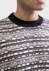 Black and white knit sweater featuring an open weave design with circular patterns, a black ribbed collar, and a textured finish.