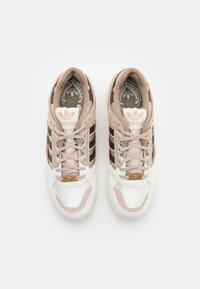 Sportovní tenisky v béžovo-hnědé barevné kombinaci, s texturovanými materiály, třemi vodorovnými pruhy a zlatým logem.