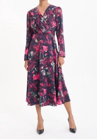 Květinové šaty v námořnické modři s růžovými a zelenými vzory. Mají dlouhé rukávy, véčkový výstřih, přiléhavý pas a rozšířenou sukni, doplněné černými podpatky.