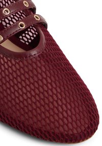 Primer plano de un zapato de tela de malla burdeos con dos correas de cuero que presentan ojales dorados en la parte superior.