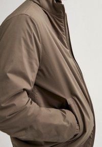 Brown padded jacket with a high collar, zip closure, and side pockets. Smooth texture with a sleek, streamlined design.