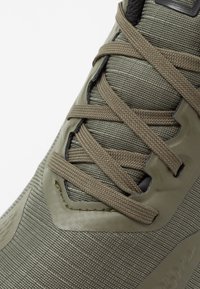 Zelená sportovní bota s texturovaným, odolným svrškem z látky, odpovídajícími šněrovadly, zesílenými očky a vrstveným designem pro podporu.