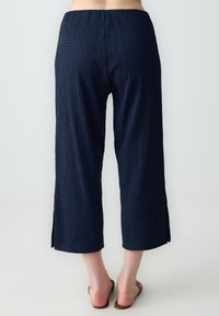 Pantalons cropped bleu marine en tissu texturé, avec fentes latérales et une taille élastique pour un ajustement confortable.