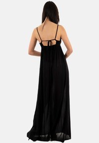 Černé maxi šaty s nastavitelnými ramínky, průhlednou tkaninou a zavazováním na zádech. Plynný silueta s lehkým, vzdušným materiálem.