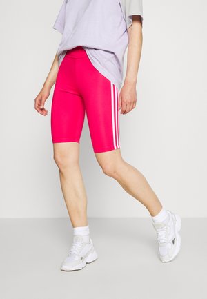 Pantaloni corte fucsia con strisce laterali bianche, realizzati in materiale elastico. Abbinati a una t-shirt larghi lavanda e scarpe da ginnastica bianche.