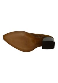 Zapato de tacón de ante marrón con punta afilada, que presenta una suela texturizada y un tacón negro en bloque. Detalle de costura sutil a lo largo de la parte superior.