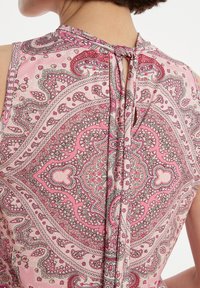 Roze paisley-patroon stof met ingewikkelde ontwerpen. Het kledingstuk heeft een halsopening aan de achterkant en een soepele, zachte textuur.