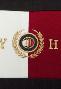 Stickad tyg med röda, vita och svarta sektioner. Har guldbroderi av en logotyp med lagerkransar och en bokstav "H."