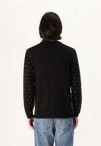 Čierny sveter s hladkým chrbtom a vzorovanými rukávmi s malými bielymi srdiečkami. Pletená štruktúra s okrúhlym výstrihom a rebrovaným lemom.