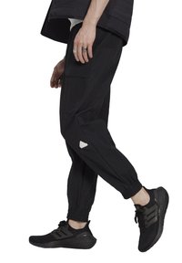 Svarta cargo byxor med sidofickor, elastiska manschetter och en liten vit logotypdetalj. Bärs med svarta träningsskor som har randiga detaljer.