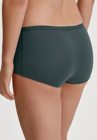 Donkergroene katoenen slip met een soepele textuur, met een brede elastische tailleband en een klassieke snit, weergegeven vanaf de achterkant met een naadloos ontwerp.