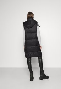 Schwarze Pufferweste mit Kapuze, gestepptem Muster und gerippten Armlöchern. Kombiniert mit eng anliegenden schwarzen Lederhosen und Ankle Boots.