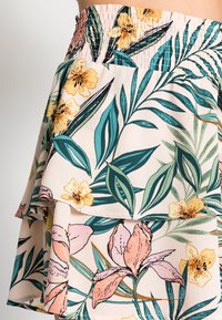 Saia floral com design de babados, confeccionada em tecido leve nas tonalidades suaves de rosa, amarelo e verde, com padrões de folhas detalhados.