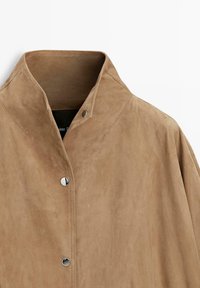 Světlohnědá semišová bunda s vysokým límcem a třemi viditelnými stříbrnými patentkami vpředu.