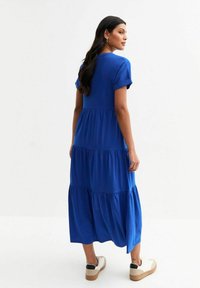 Blue tiered maxi dress with short rolled sleeves and a relaxed fit. The fabric is soft, with a smooth texture and flowy silhouette.