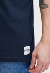 Tamno plava pamučna majica s bočnom etiketom "NORTH BEND." Ima klasičan okrugli izrez i kratke rukave te teksturiranu tkaninu.