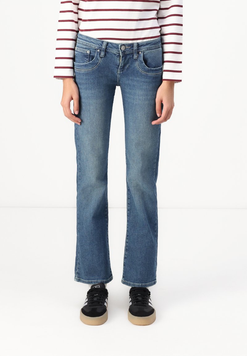Blue denim jeans with a straight leg design, featuring front pockets and a button closure. Worn with black sneakers.