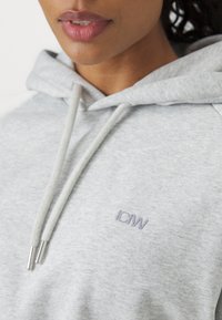 Felpa grigia con cappuccio caratterizzata da una texture morbida, cordini regolabili con punte in argento e un piccolo logo "IDW" ricamato sul petto.