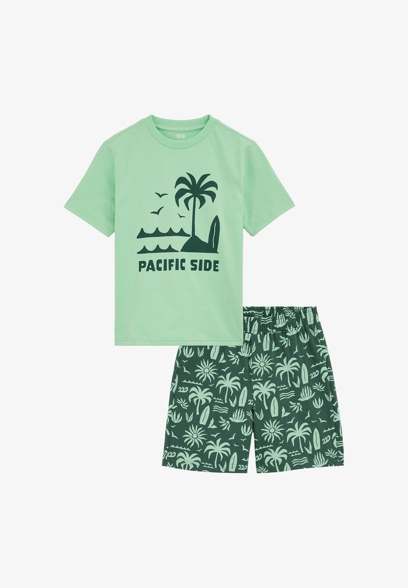 Zelena pamučna majica kratkih rukava s crnim natpisom "PACIFIC SIDE" i palmom; odgovarajuće kratke hlače sa zelenim tropskim uzorkom i elastičnim pojasom.