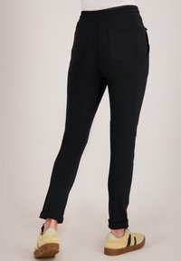 Zwarte joggerbroek met taps toelopende pasvorm, elastische tailleband en omgeslagen boorden. Voorzien van twee achterzakken en een gladde stoftextuur.