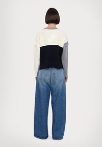 Gehaakte sweater met een gestructureerd ontwerp, in crème, marineblauw en grijs. Gecombineerd met losse blauwe spijkerbroek, wat zorgt voor een casual uitstraling.