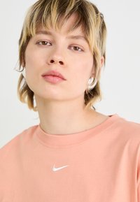 Peach cotton T-shirt with a crew neckline and a white Nike logo on the left chest. Soft texture with minimalistic design.