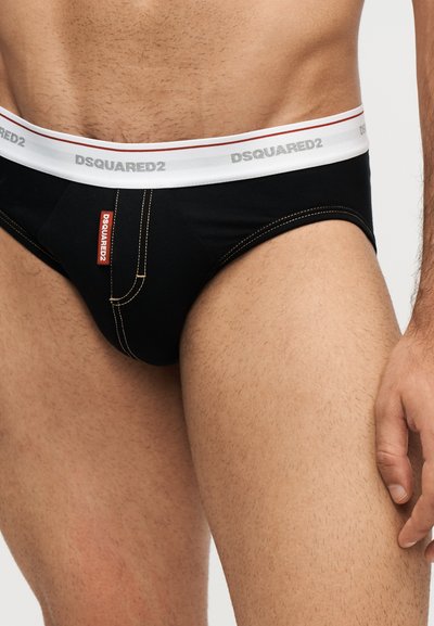 Mannequin masculin portant un slip noir avec une ceinture blanche ornée du logo DSQUARED2 en gris et une étiquette rouge à l'avant gauche.