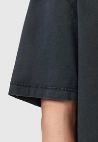 Czarny bawełniany t-shirt o nieco oversize'owym kroju, z surowym wykończeniem rękawów i widocznymi detalami ściegów.
