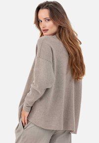 Pull gris clair surdimensionné avec une texture douce, épaules tombantes et fentes latérales. Associé à un pantalon ample de couleur claire.