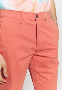 Chinos corallo caratterizzati da una morbida miscela di cotone, taglio dritto, cuciture visibili e chiusura con bottone in vita.